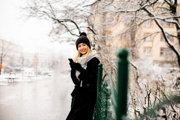 Young woman n warm clothes enjoying in snow and using mobile phone