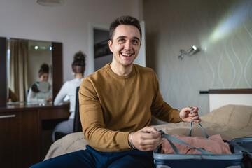 Man caucasian couple packing or unpack wardrobe cloth from suitcase at hotel room while his wife or girlfriend sit in background travel and vacation concept copy space
