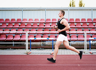 Obraz premium Young muscular fit male sprinter running on a red running track - Fitness and wellness concept with a millennial runner - Copyspace on the photo's left side