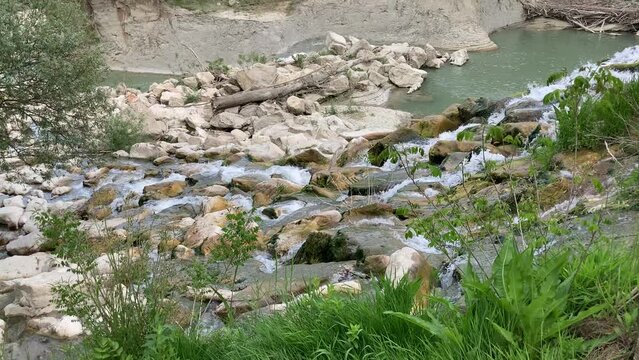 Fair view from above at fresh vivid streams of the Tenna river descending through the sturdy rocks with a tree branch and some green grass in the foreground and an abrupt riverbank in the background