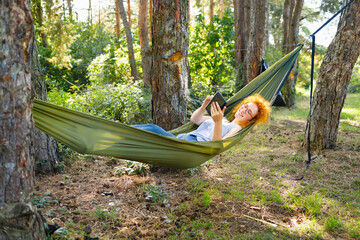 Young woman camping and reading in a hammock