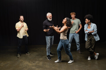 multiracial woman gesturing while rehearsing near bearded art director and smiling interracial...