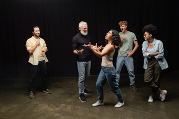 multiracial woman gesturing while rehearsing near bearded art director and smiling interracial actors.