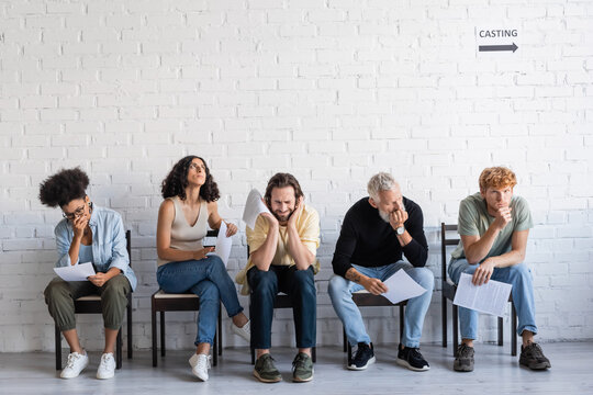 worried and thoughtful multiethnic actors sitting with screenplays and waiting for casting in corridor.