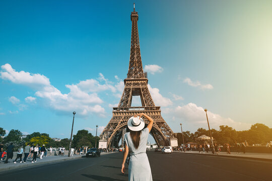 Rear View Of Woman Tourist In Sun Hat Standing In Front Of Eiffel Tower In Paris. Travel In France, Tourism Concept. Holiday Or Vacation In Paris