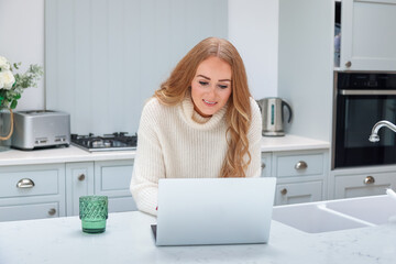 Fototapeta na wymiar Beautiful middle age woman with laptop working from home online at her cozy kitchen