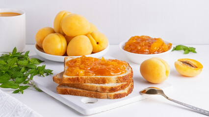 Toasts of bread with apricot jam and fresh fruits with mint on white wooden table. Tasty breakfast
