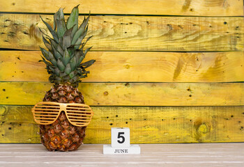 Creative june calendar planner with number  5. Pineapple character on bright yellow summer wooden background with calendar cubes.