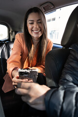 woman inside the back of a car, transport by cab or car with driver, showing her mobile phone to the driver to ask for directions. she is traveling for work with orange blazer and cream sweater