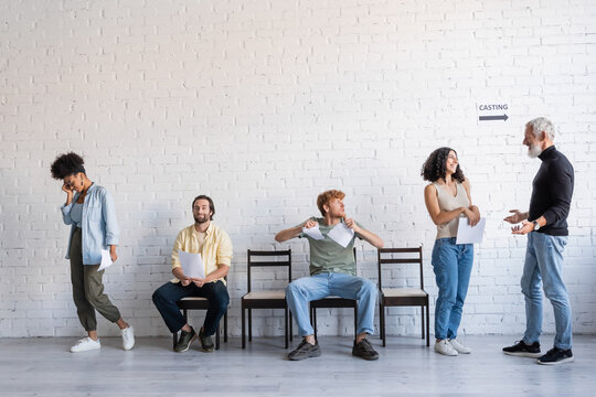 grey haired producer talking to happy multiracial woman near upset multiethnic job seekers.