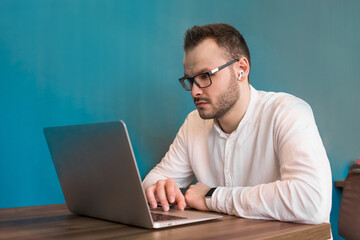 Attractive guy young European businessman works in a laptop sitting at a table in a cafe