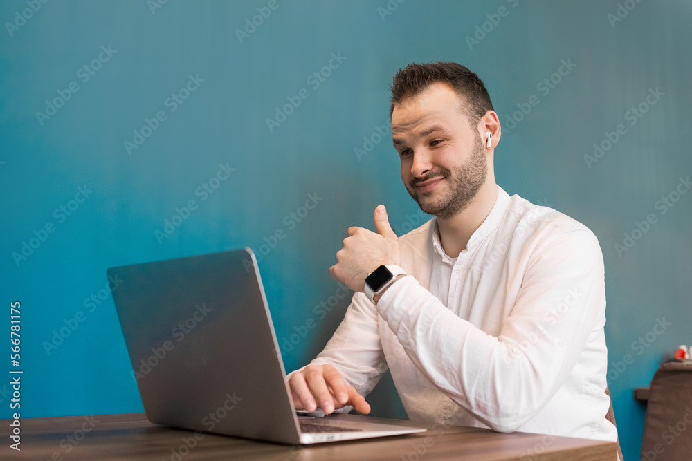 Wall mural a young attractive businessman guy with a beard works in a laptop sitting at a table in a cafe and s