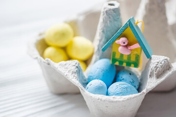 A bunch of yellow and blue eggs in egg carton. near the house with a bird. The concept of an abandoned home of Ukraine for the Easter holiday.