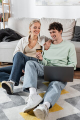 cheerful man holding credit card while using laptop near smiling girlfriend.