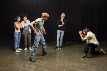 young actors playing scene near grey haired art director and amazed interracial women. Translation...