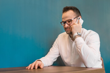 Stylish attractive young European guy businessman in glasses and white shirt talking on mobile phone