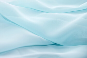 Texture of a wavy surface of a pastel blue chiffon fabric as a background. Photo in perspective