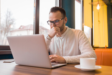 Stylish busy business businessman of European appearance works in a laptop for a cup of coffee in a cafe