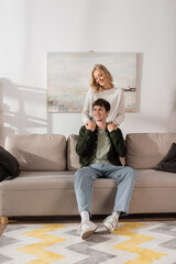 young cheerful woman in sweater hugging boyfriend in living room.