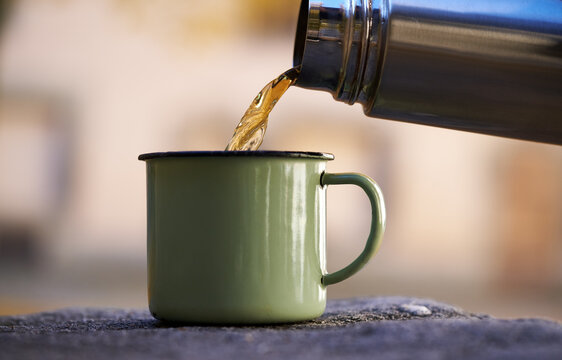 Pouring tea from a vacuum flask into a cup, outdoors
