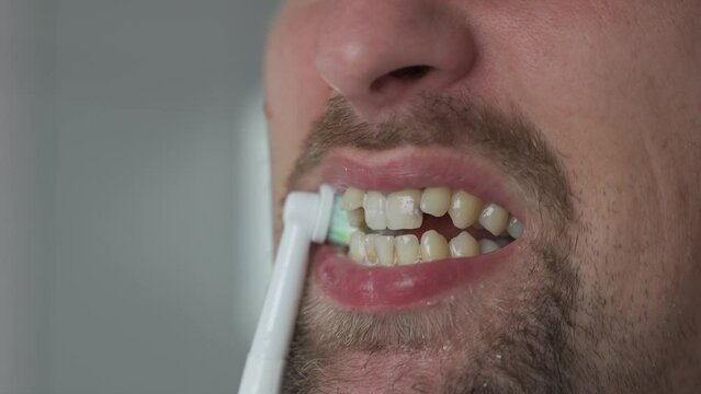 Theme of brushing and whitening teeth with a modern electric toothbrush. Close-up of a man cleaning his teeth with an ultrasonic dental brush. Morning routine, oral hygiene. Oscillating toothbrush. 
