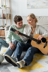 cheerful blonde woman playing acoustic guitar near curly boyfriend.