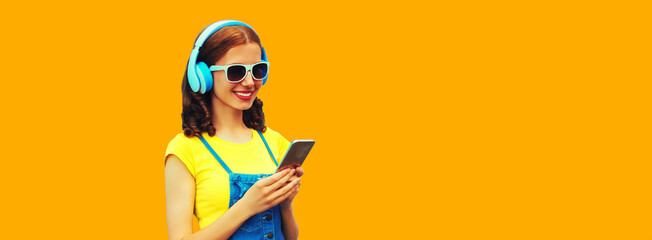 Portrait of smiling young woman in headphones listening to music with smartphone on yellow background, blank copy space for advertising text