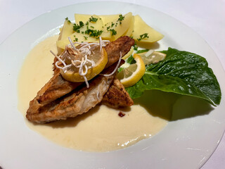 Ein Teller mit Fischfilet, Kartoffeln und einer sauren Soße.