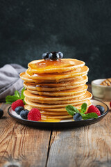 Delicious pancakes, with fresh blueberries, raspberry and maple syrup or honey on a dark background