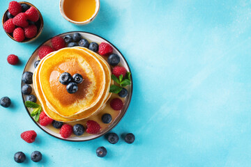 Delicious pancakes, with fresh blueberries, raspberry and maple syrup or honey on a dark background