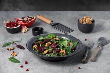 Healthy green salad with fresh spinach, brie cheese, walnuts, pomegranate on grey stone table. Vegetarian food concept. Food recipe background. Close up.