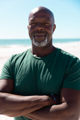 Portrait of bald confident african american senior man with arms crossed at beach under clear sky