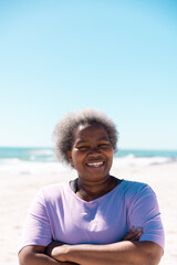 Smiling african american senior woman with short hair and crossed arms standing against sea and sky