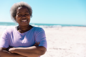 African american senior woman with arms crossed standing against sea and clear sky, copy space