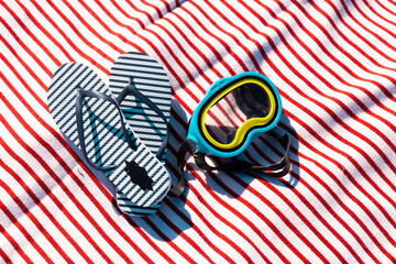 High angle view of blue flip-flops and swimming googles on beach towel during sunny day