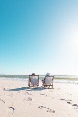 African american senior couple relaxing on deckchairs in front of sea under clear blue sky