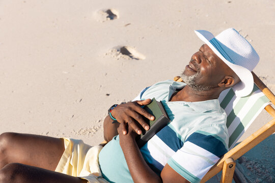 High Angle View Of African American Senior Man Wearing Hat With Eyes Closed Relaxing On Deckchair