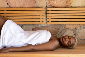 Fototapeta na wymiar Happy african american woman wearing towel and lying in sauna