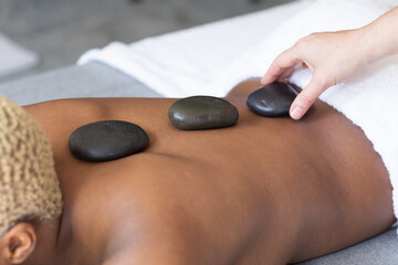 Hand putting hot stones on african american woman's back