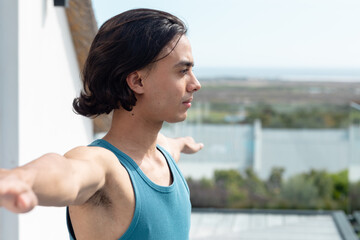 Happy biracial man doing yoga, stretching on balcony