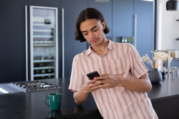 Happy biracial man using smartphone in kitchen