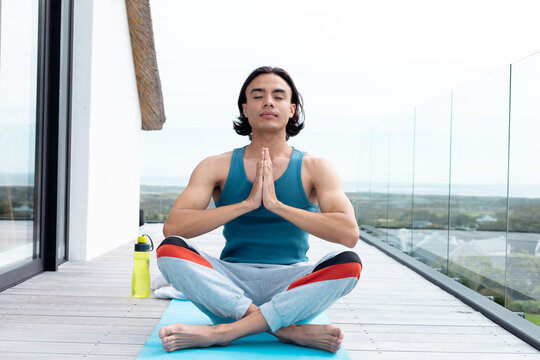 Happy biracial man doing yoga, meditating on balcony - Powered by Adobe