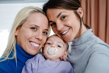 Gay lesbian couple and newborn baby taking selfie picture indoors at home - Lgbt family concept -...