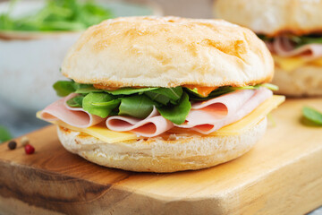Two homemade sandwiches with ham, cheese and arugula on a concrete table.