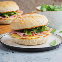 Two homemade sandwiches with ham, cheese and arugula on a concrete table.