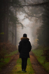 Frau, die in dichtem Nebel in einem Wald spazieren geht.