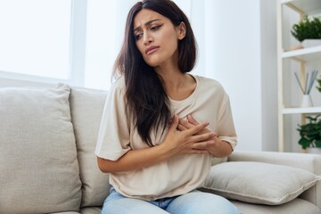 Obraz premium Woman sitting on sofa at home arm and shoulder pain, muscle sprain and joint pain, calcium problems in bones