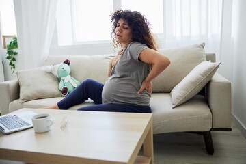 Pregnant woman sitting on the couch lower back pain and headache, strain on the spine during pregnancy. Lifestyle preparation for childbirth, last month of pregnancy