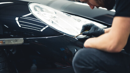 Gentle black car paint touch-ups done with a small brush in the area of headlights. Focused car detailing expert during work. High quality photo