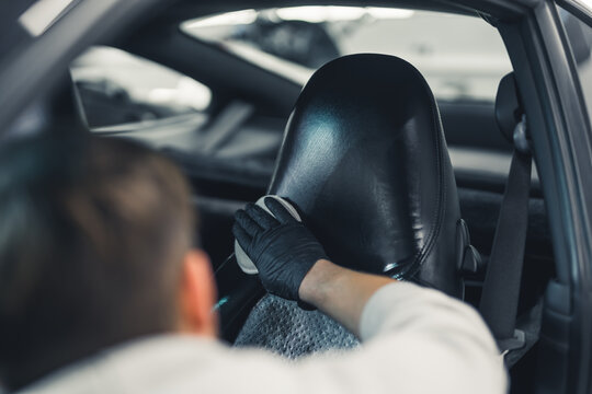Car detailing process - dust removing. Unrecognizable male expert cleaning leather car seats with white cotton pad. Blurred person in the foreground. High quality photo